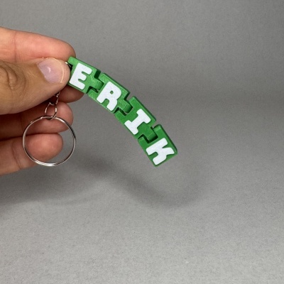 Chaveiro de madeira verde com letras brancas ERTH a ser segurado por uma mão sobre fundo cinzento.