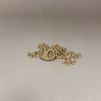 Figura de sapo bege em plástico com textura e design de ossos sobre fundo cinza.