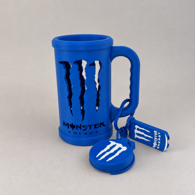 Caneca e chaveiros azuis com logótipo Monster Energy sobre fundo cinzento