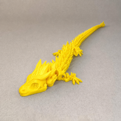 Figura amarela de dragão de plástico com textura detalhada e espinhos sobre superfície cinzenta