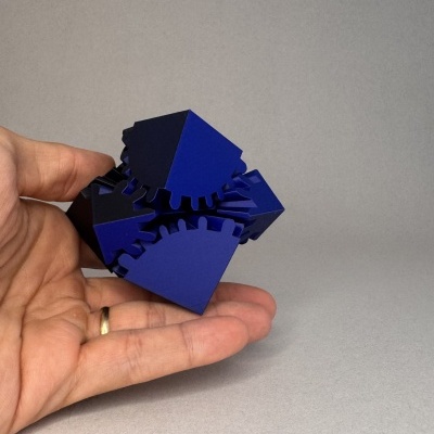 Objeto geométrico azul e preto com engrenagens na mão de uma pessoa