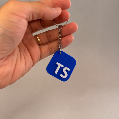 Porta-chaves azul com letras brancas TS segurado à mão com fundo cinzento.