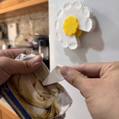 Clip magnético em forma de flor branco e amarelo a fechar saco plástico na cozinha.