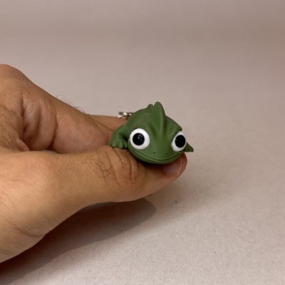 Boneco lagarto verde com grandes olhos segurado por uma mão