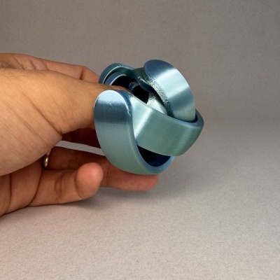 Objeto metálico azul entrelaçado segurado por mão sobre fundo cinzento
