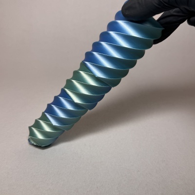 Escultura espiralada azul e verde metálica segurada por mão com luva preta