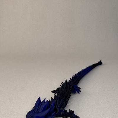 Escultura de dragão preto e azul com textura estriada numa superfície clara