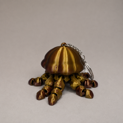 Chaveiro em forma de polvo metálico dourado e bronze sobre fundo cinza claro