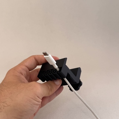 Mão segurando peça preta com cabo branco USB-C contra fundo bege
