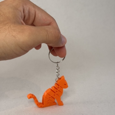 Porta-chaves de gato laranja articulado sendo segurado por mão com fundo branco.