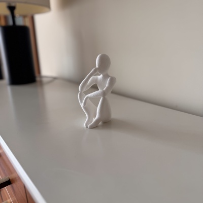 Estatueta decorativa branca em forma de figura humana sentada numa superfície branca