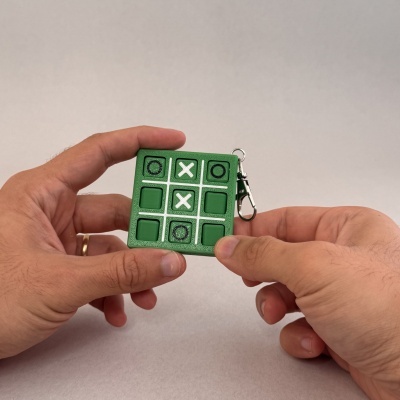 Chaveiro verde jogo da velha com símbolos X e O em mãos sobre fundo cinzento