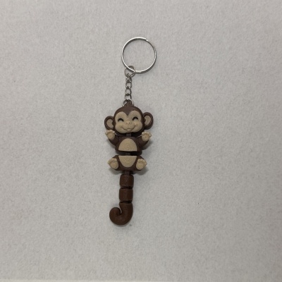 Chaveiro de plástico em forma de macaco castanho e bege sobre fundo cinza