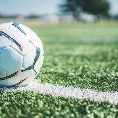 Bola de futebol branca com padrões e logótipo Puma sobre relvado artificial.