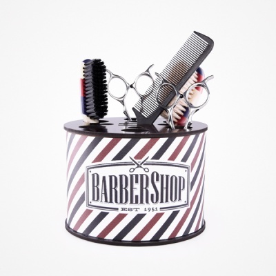 Conjunto de ferramentas para barbearia com escova, tesouras e pente numa base preta e branca listrada com texto 'BARBERSHOP'.