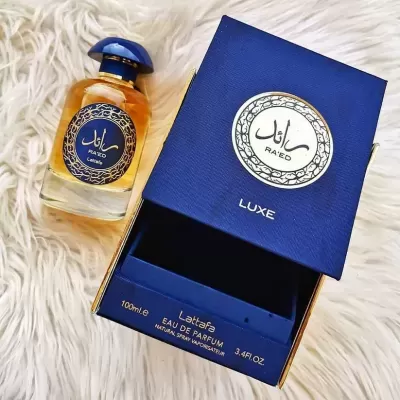Frasco de perfume com caixa azul escuro e detalhes dourados sobre superfície branca felpuda