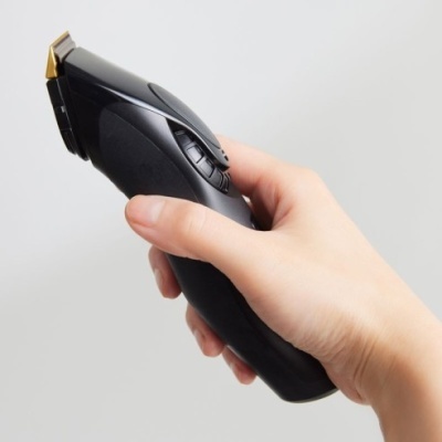 Máquina de cortar cabelo preta com lâmina dourada na mão