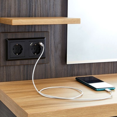 Tomada elétrica dupla na parede com cabo branco ligado a smartphone na mesa de madeira