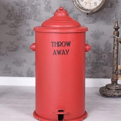 Lixeira vermelha metálica com texto 'THROW AWAY' em fundo de sala com relógio e parede cinzenta