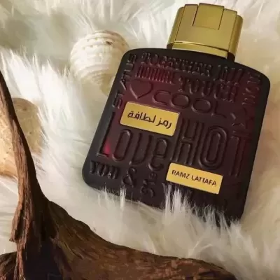 Frasco de perfume preto com tampa dourada sobre tecido branco felpudo e conchas