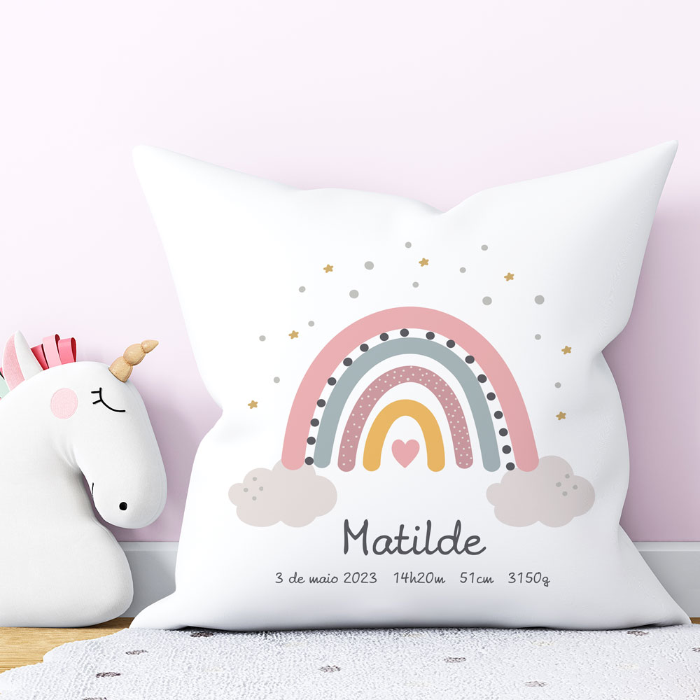 Almofada branca com estampa de arco-íris e dados de nascimento ao lado de peluche unicórnio