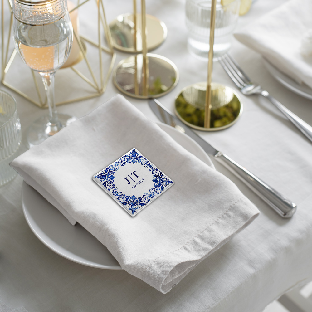 Guardanapo branco em tecido com cartão azul e branco JTT sobre prato branco numa mesa posta elegante