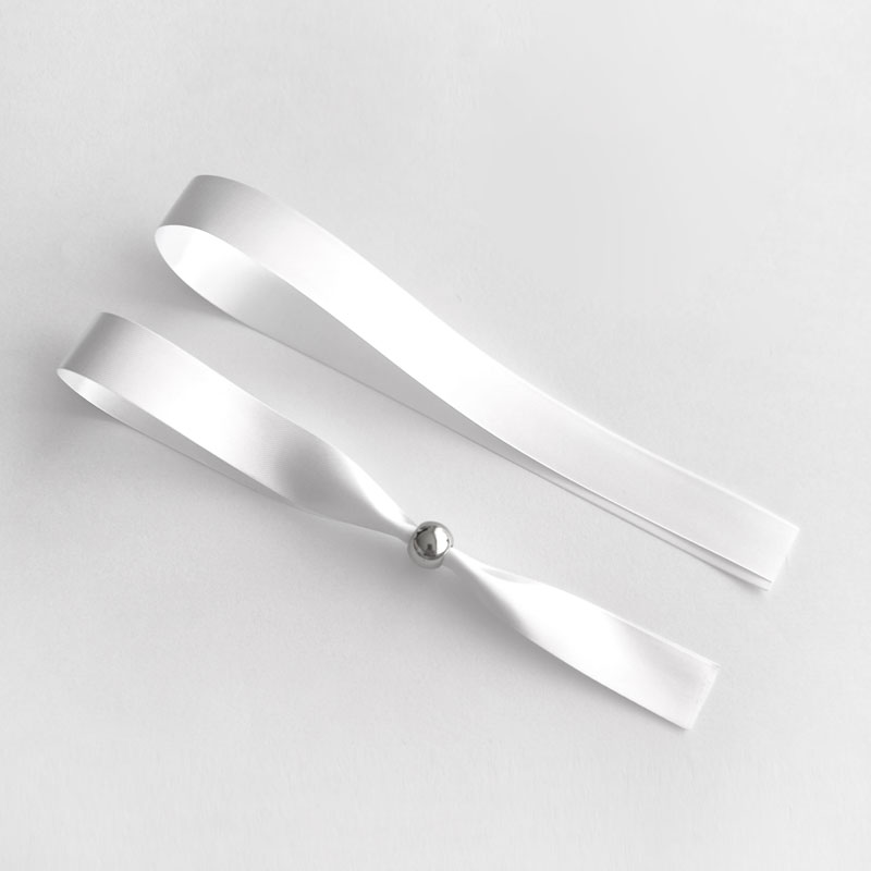 Duas fitas brancas de cetim em fundo branco, uma com esfera metálica
