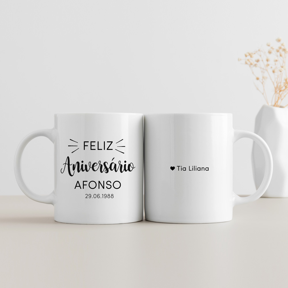 Conjunto de duas canecas brancas com escrita preta, decoradas com textos de feliz aniversário e nome, sobre superfície clara com vaso branco ao fundo.