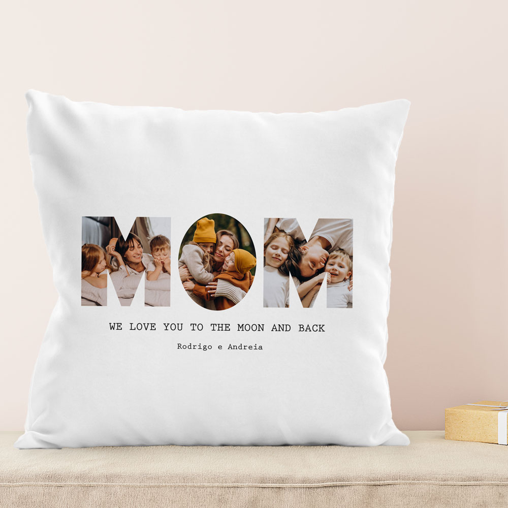 Almofada branca com letras MOM e texto em preto, sobre superfície clara e fundo bege
