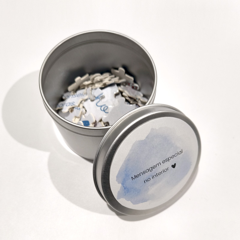 Caixa metálica prateada aberta com peças de puzzle e tampa com etiqueta azul e texto