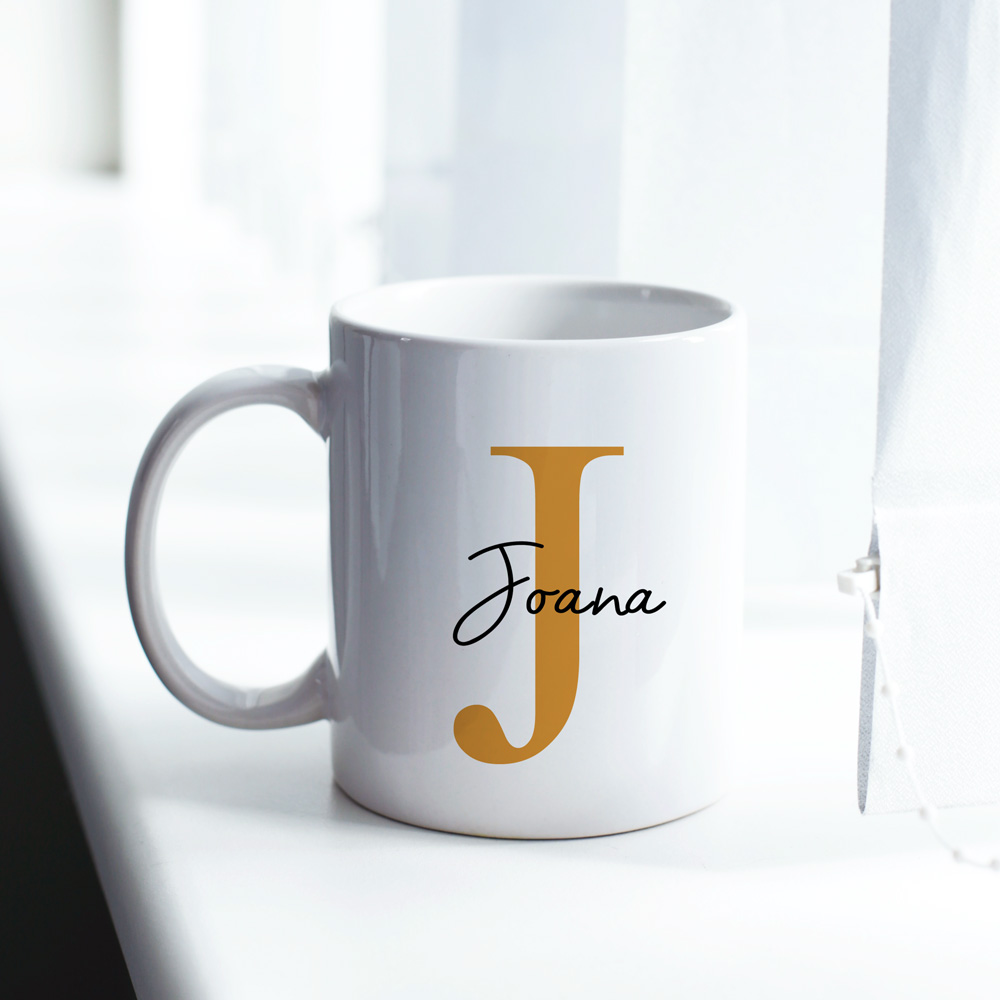 Caneca branca com letra J dourada e nome Joana preto junto a janela com cortinas brancas