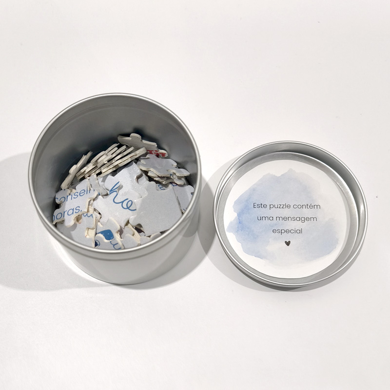 Puzzle de peças de cartão em caixa metálica prateada com tampa contendo mensagem