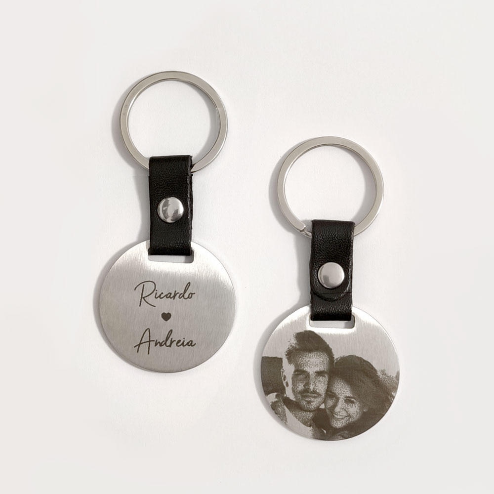 Dois porta-chaves redondos em metal prateado com tira preta, um com nomes gravados e outro com fotografia de casal.