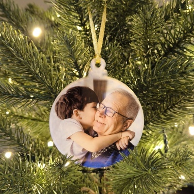 Ornamento circular com foto de criança beijando idoso pendurado numa árvore de Natal