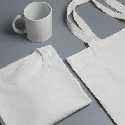 Conjunto de camiseta, mala de tecido e caneca, todos brancos sobre fundo cinzento