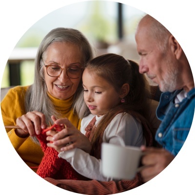 Três pessoas juntas, mulher idosa a fazer tricot vermelho, menina e homem idoso com caneca branca