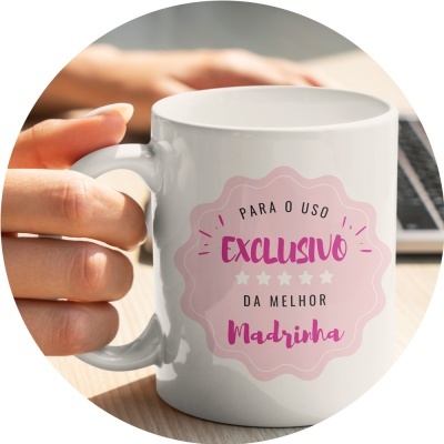 Caneca branca com texto em rosa e preto segurada por uma mão junto a um portátil.