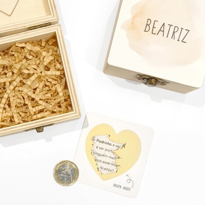 Caixa de madeira aberta com papel de enchimento, moeda de 1 euro e cartão com coração dourado e texto raspado