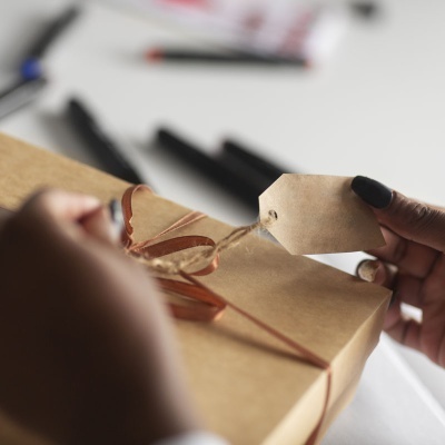 Embalagem de presente em papel castanho com fita e etiqueta de papel castanho sendo segurada