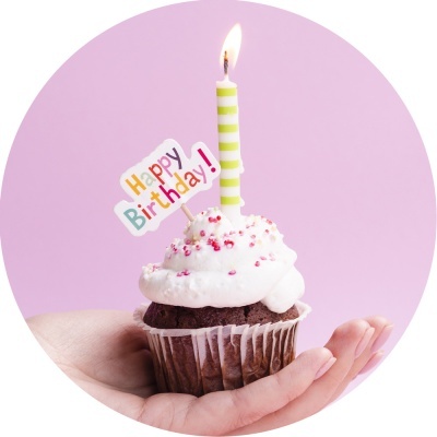 Cupcake com vela acesa e placa 'Happy Birthday!' em fundo rosa