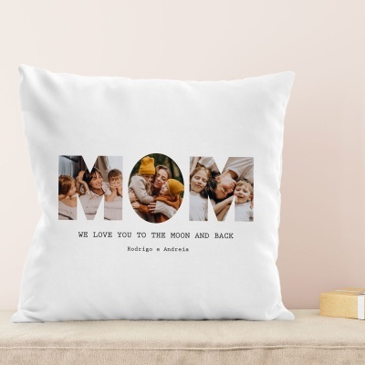 Almofada branca com letras MOM e texto em preto, sobre superfície clara e fundo bege