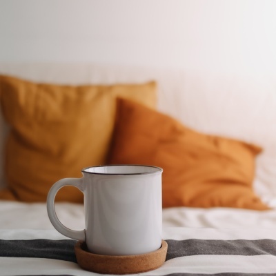 Caneca branca de cerâmica com suporte de cortiça sobre tecido listrado cinza e branco