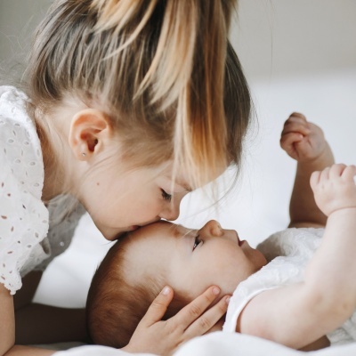 Criança beijando a testa de um bebé deitado, com roupa branca