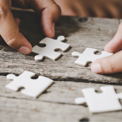 Peças de puzzle brancas sobre mesa de madeira com mãos a segurar duas peças
