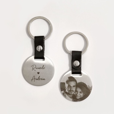 Dois porta-chaves redondos em metal prateado com tira preta, um com nomes gravados e outro com fotografia de casal.