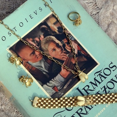 Conjunto de joias douradas com abelhas sobre livro azul com texto em português