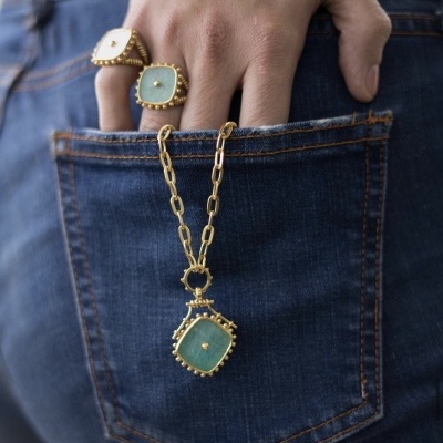Anéis dourados e colar com pedras verdes e brancas em bolso de jeans azul