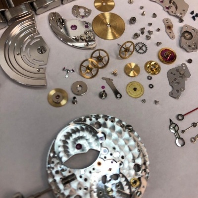 Peças metálicas desmontadas de um relógio mecânico numa superfície branca