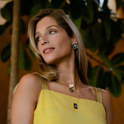 Colar e brincos dourados com pendentes azuis e estrelas em mulher com vestido amarelo