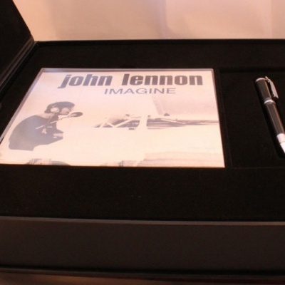 Caixa preta com livro ou CD 'john lennon IMAGINE' e uma caneta preta